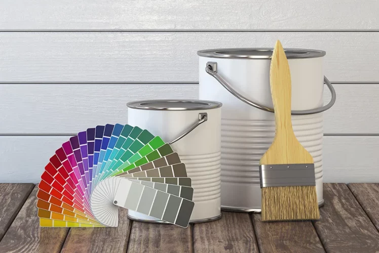 Paint cans, a brush and a color palette laid out on wood