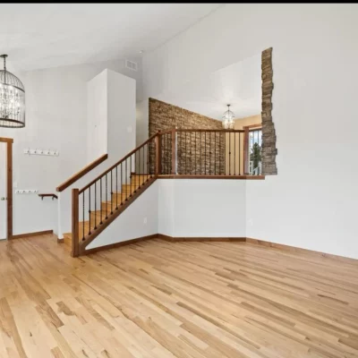 Open room with light hardwood and a wood staircase beside a stone wall